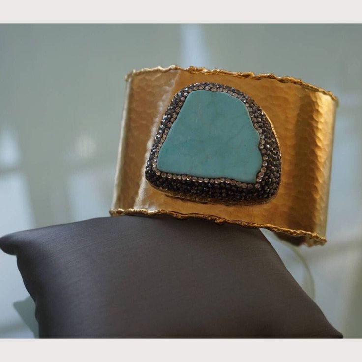 Hammered gold plated cuff with turquoise stone and black and white Swarovski crystals surrounding the stone. Cuff is adjustable to fit most wrist sizes. Ships in a drawstring pouch. Adjustable Turquoise Bracelet With Gemstone Accents, Adjustable Turquoise Luxury Jewelry, Adjustable Luxury Turquoise Jewelry, Luxury Adjustable Turquoise Jewelry, Gold Cuff Bracelet Bangle With Stones, Gold Stone Bangle Cuff Bracelet, Gold Cuff Bracelet With Stones, Red Bangles, Turquoise And Gold