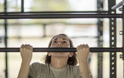 a woman is hanging on the bars in a crossfit gym with her hands behind her head