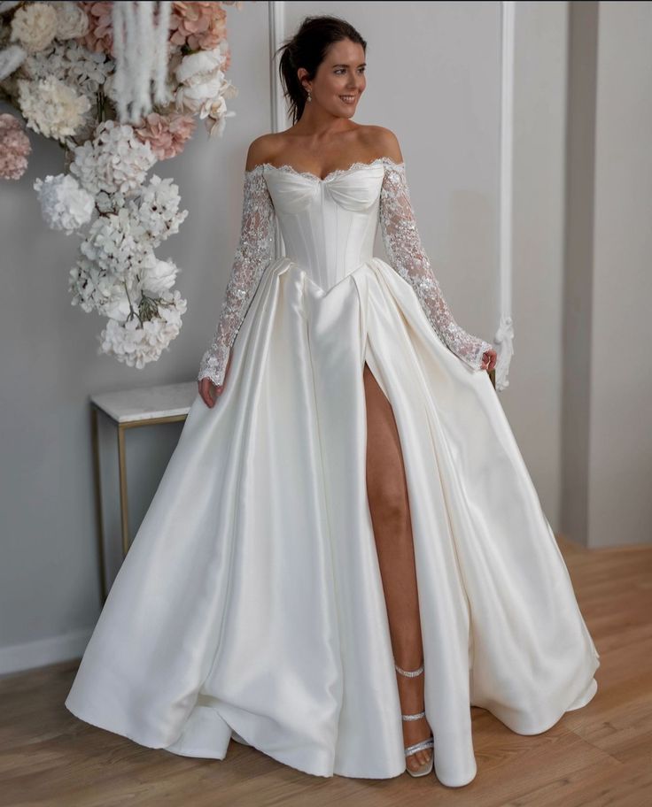 a woman wearing a white wedding dress with long sleeves and a slit down the side