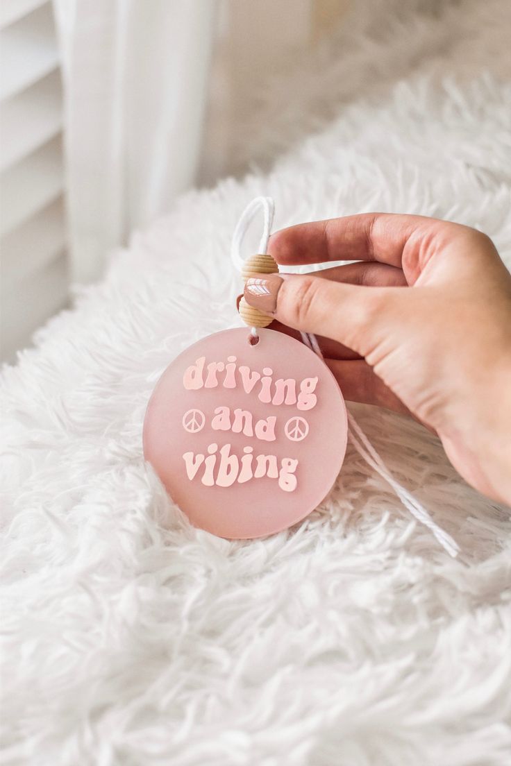 a hand holding a pink ornament that says driving and vibing on it