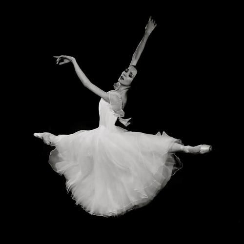 a ballerina in the air with her arms outstretched and legs spread out, wearing a white tulle