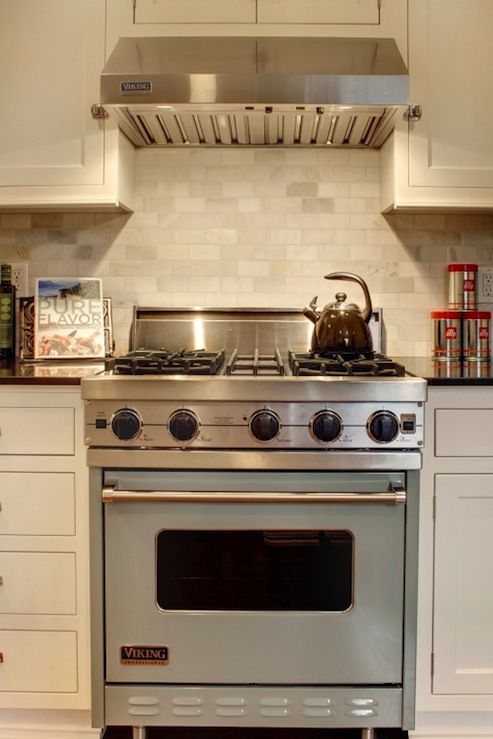 a stove top oven sitting inside of a kitchen next to white cupboards and drawers