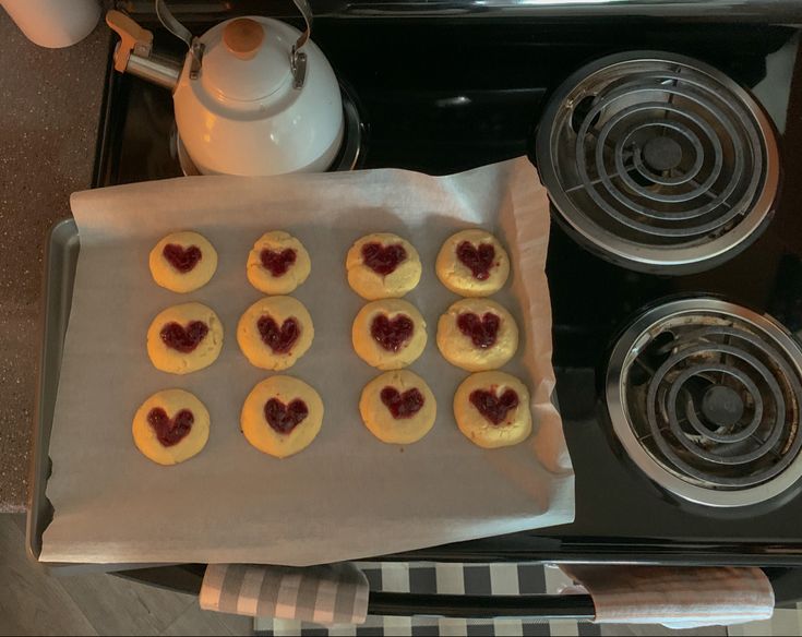 small heart shaped cookies are on a baking sheet next to an electric stove and tea kettle