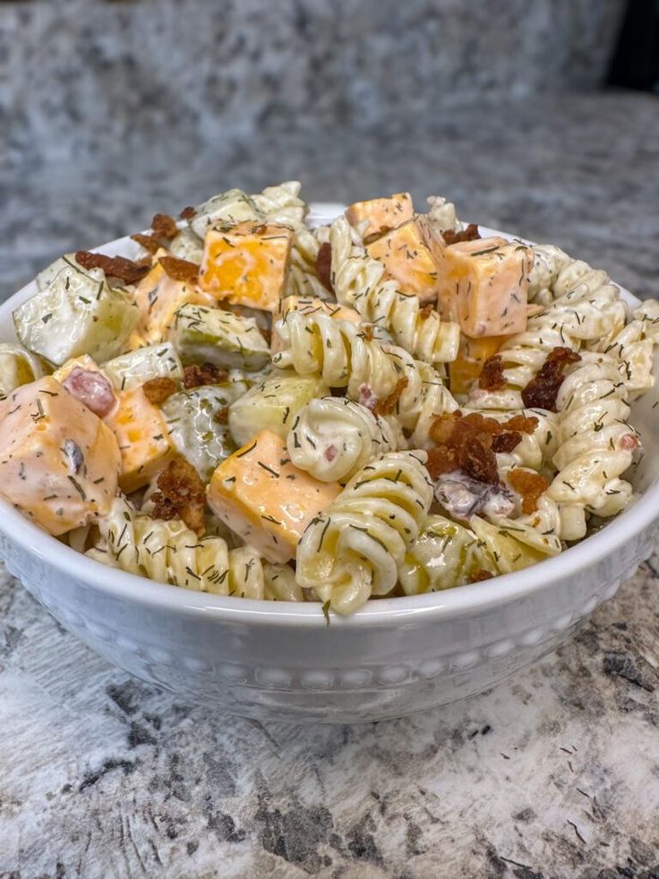 a white bowl filled with pasta salad on top of a marble counter next to a bottle of wine