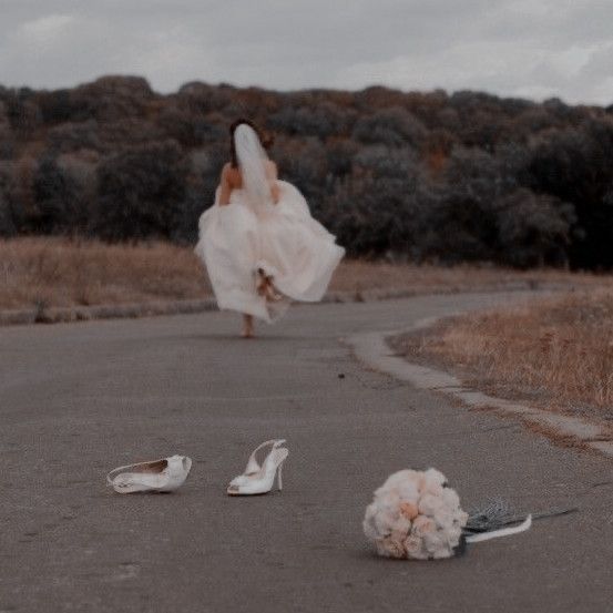 a woman is walking down the road with her dress blowing in the wind and shoes on the ground