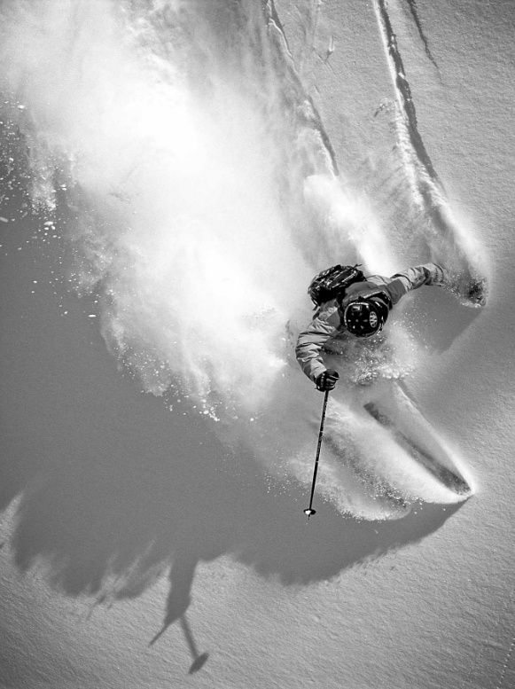 a man riding skis down the side of a snow covered slope with powder behind him