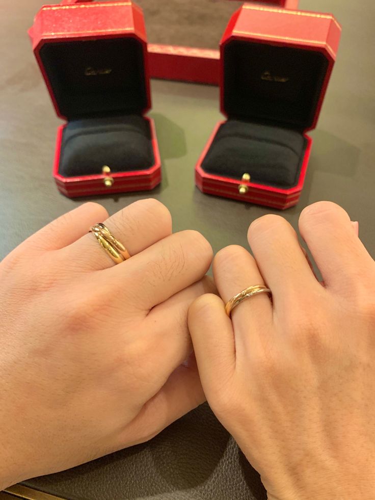 two hands holding wedding rings in front of an open red ring box on a table