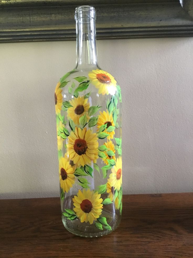 a glass bottle with sunflowers painted on it sitting on top of a wooden table