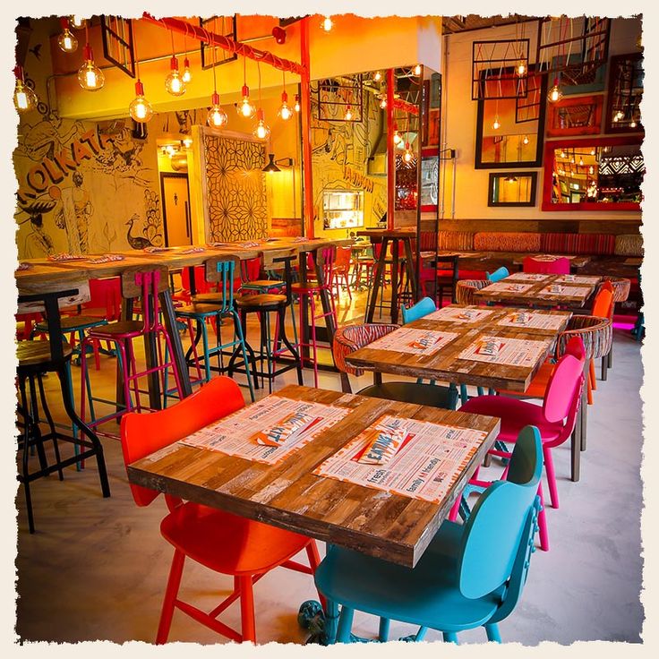 an empty restaurant with colorful chairs and tables in the foreground, lit by hanging lights