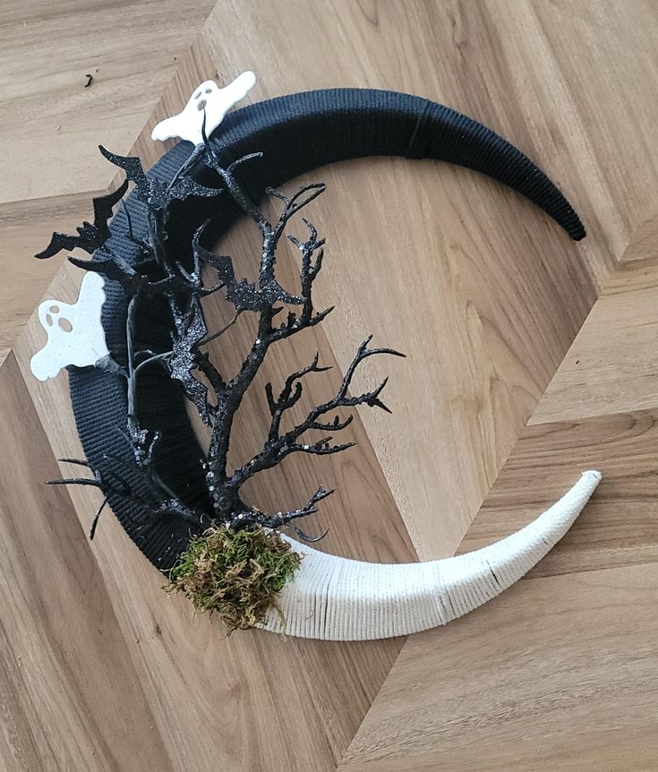 a black and white halloween wreath on top of a wooden floor next to a dead tree