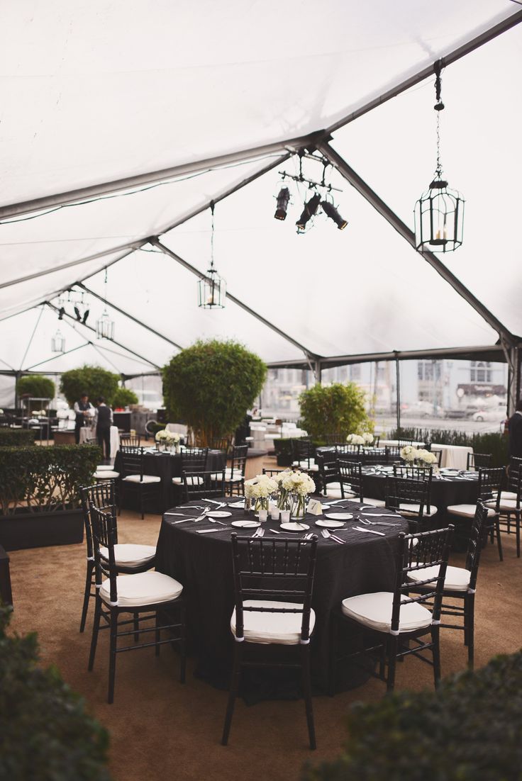 tables and chairs are set up for an event under a tent with lights hanging from the ceiling