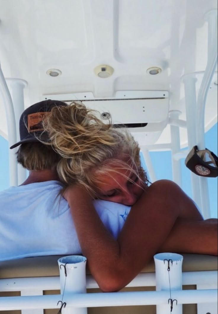 two people sitting on a boat with their arms around each other and one person wearing a hat