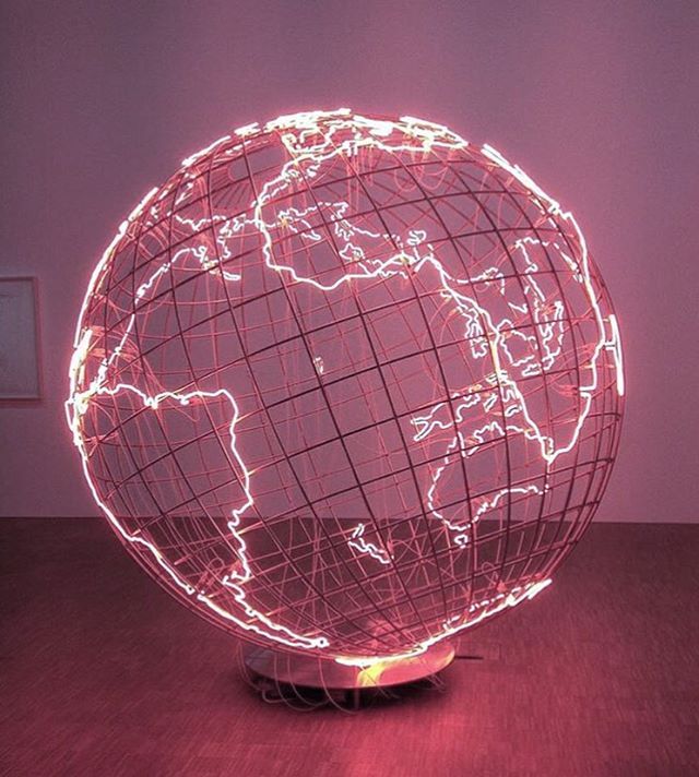 an illuminated globe on a wooden table in front of a pink wall with the world map