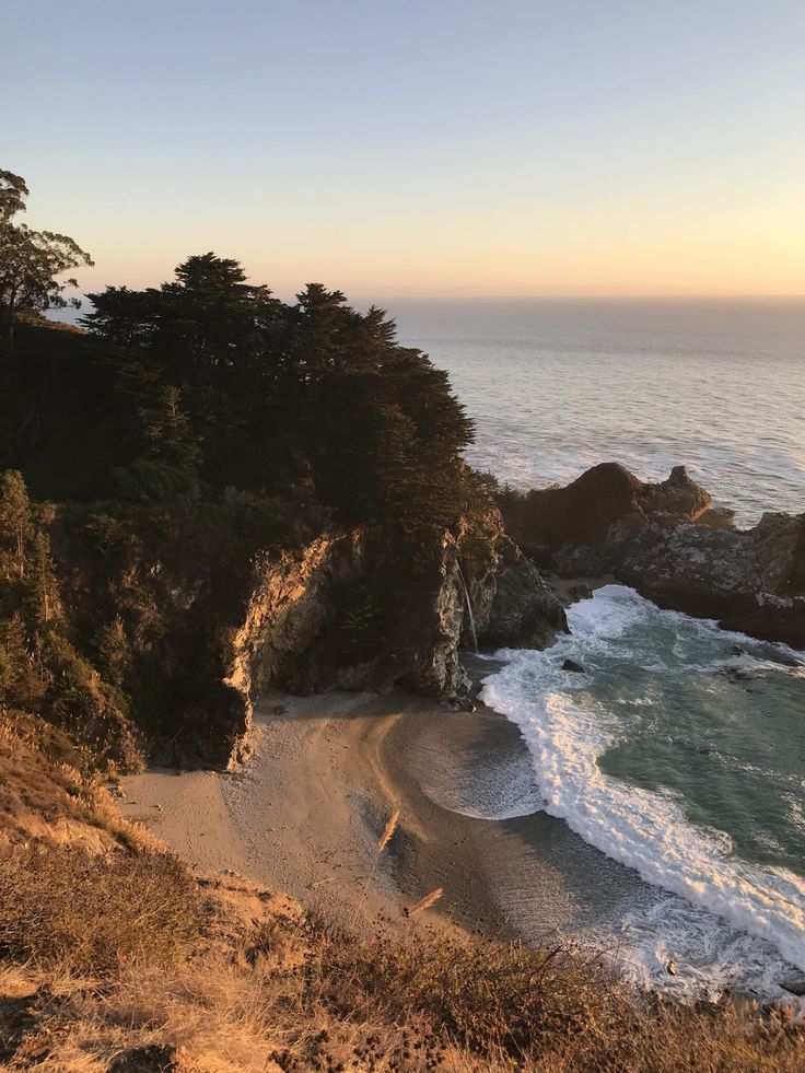 the beach is next to some trees and waves in the ocean at sunset or sunrise