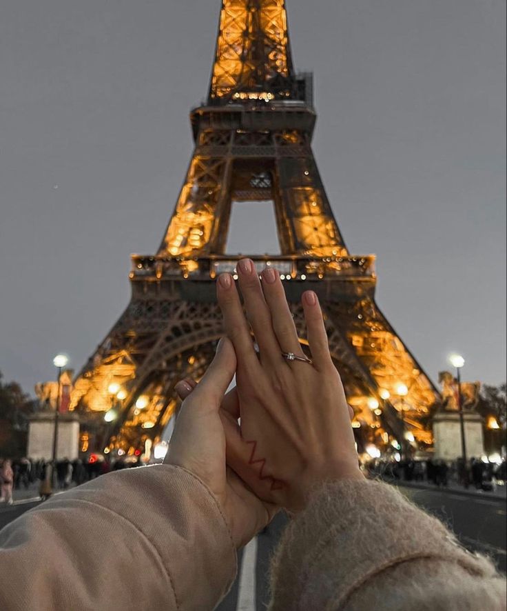 two people holding their hands up in front of the eiffel tower at night