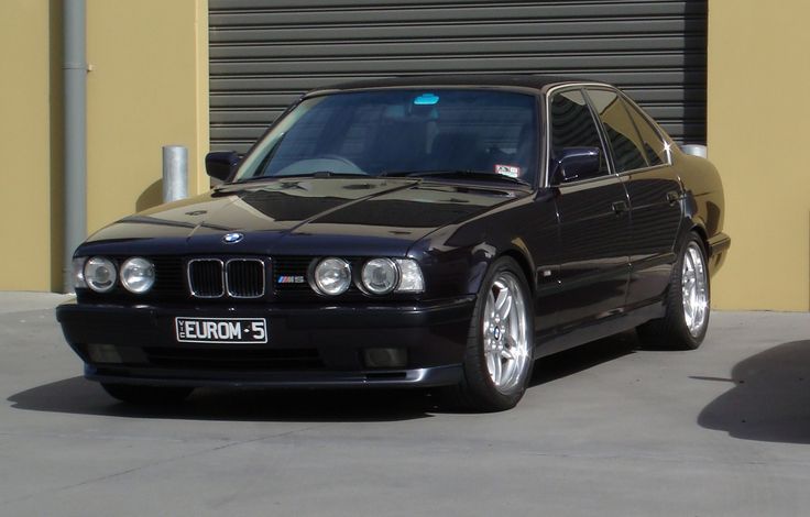 a black bmw is parked in front of a garage with its door open and it's lights on