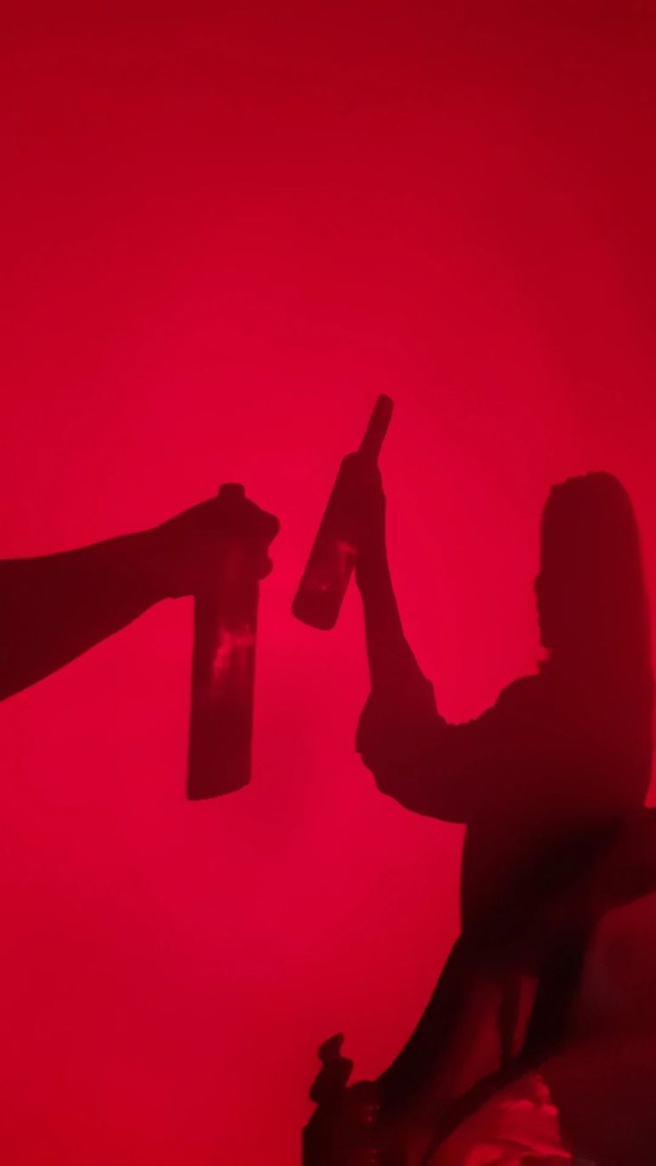 two people holding wine bottles in their hands while sitting on a couch against a red background