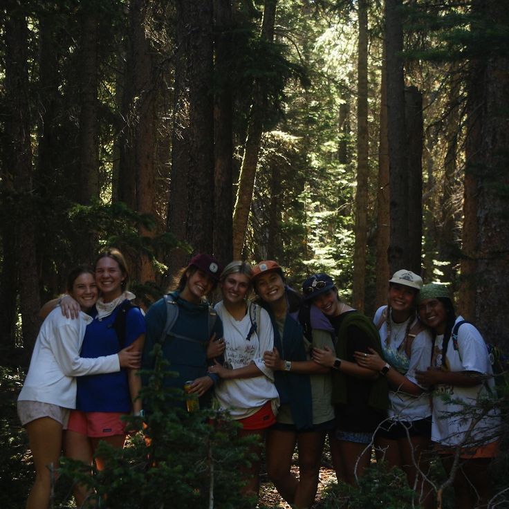 a group of young women standing in the woods hugging each other and smiling at the camera