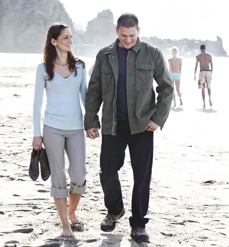 a man and woman walking on the beach holding hands