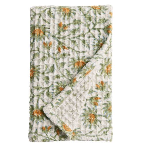 an orange and green blanket folded on top of a white tablecloth with floral designs