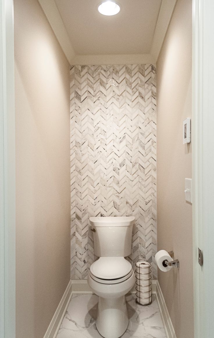 a white toilet sitting inside of a bathroom next to a roll of toilet paper on the floor