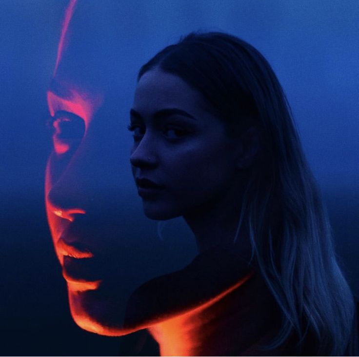 a woman standing next to a man with red light on his face in the dark