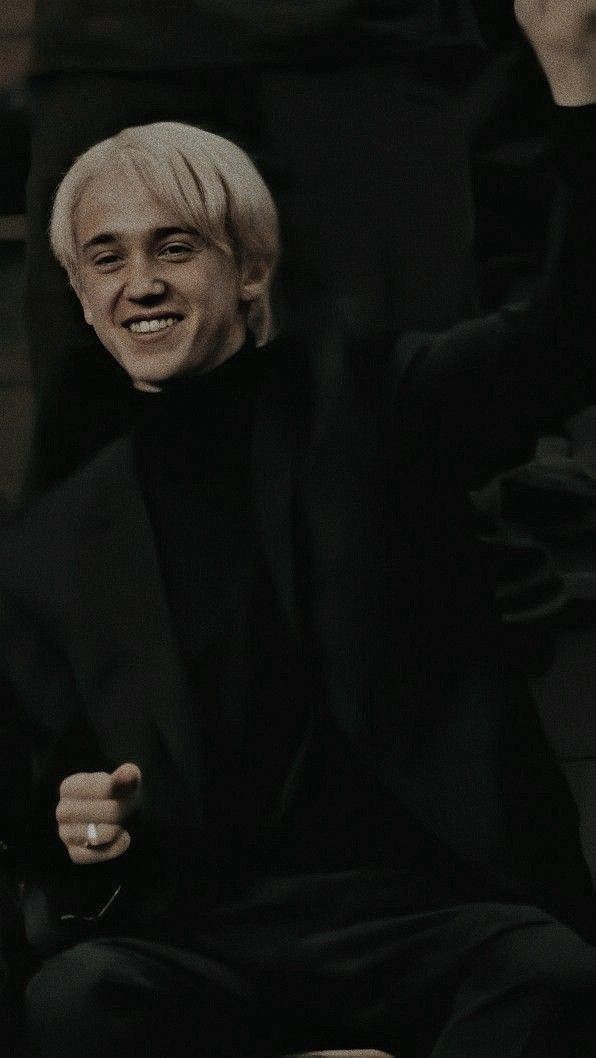 a man with white hair sitting in a chair and smiling at the camera while wearing a black suit