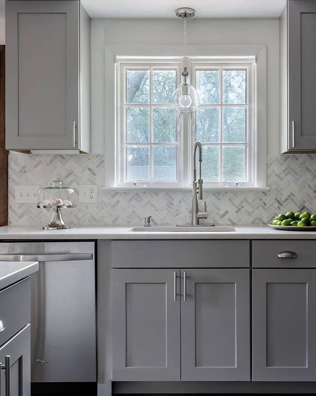 a kitchen with gray cabinets and white marble counter tops is pictured in this image, there are two windows above the sink