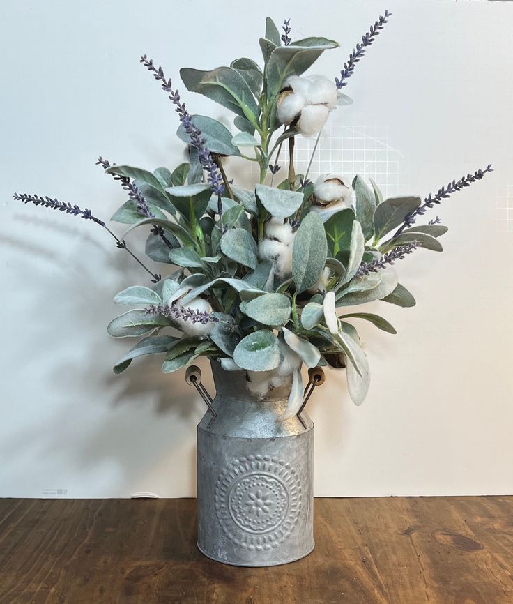 a vase filled with flowers and greenery on top of a wooden table