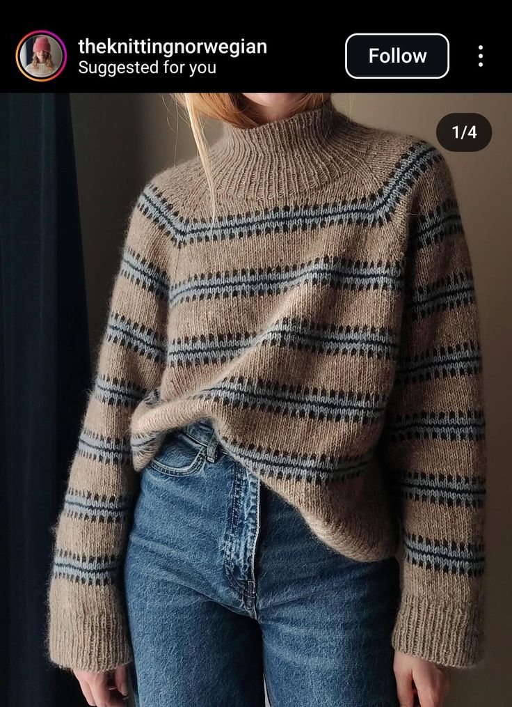 a woman wearing a sweater and jeans standing in front of a window with her hands on her hips