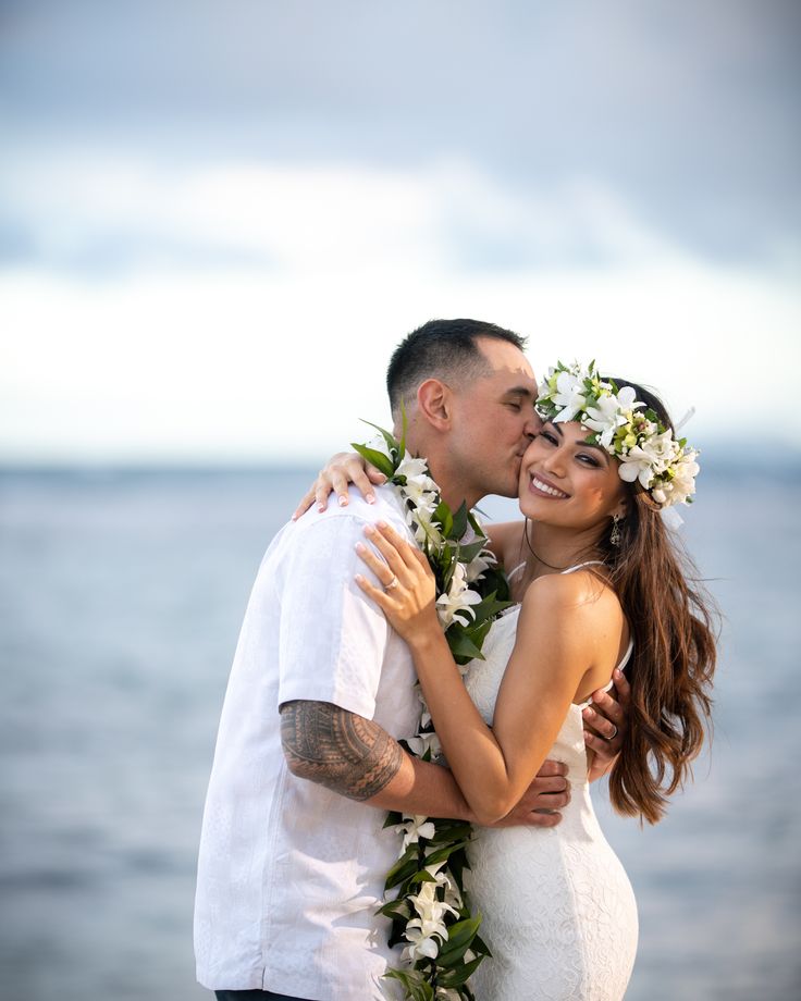 a man and woman standing next to each other in front of the ocean with flowers on their head