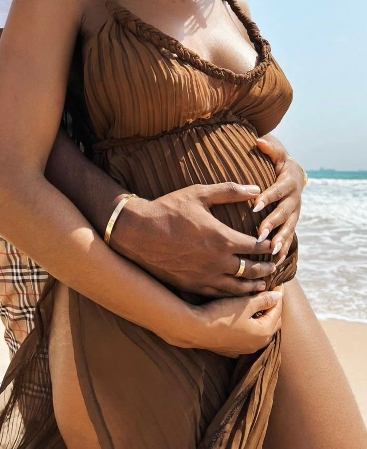 a pregnant woman sitting on the beach with her belly wrapped around her waist and hands under her stomach