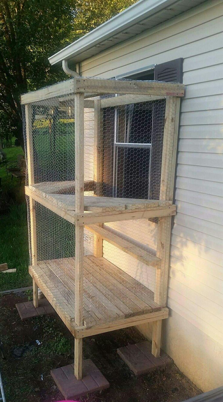 a bird cage sitting on top of a wooden shelf next to a white house in the grass