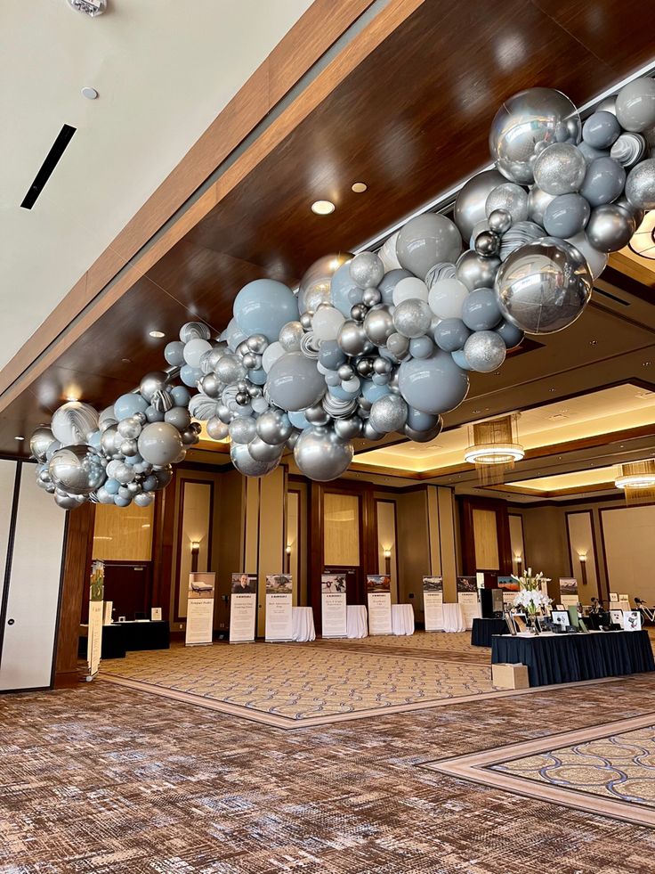 a large room filled with lots of silver and white balloons hanging from the ceiling over tables