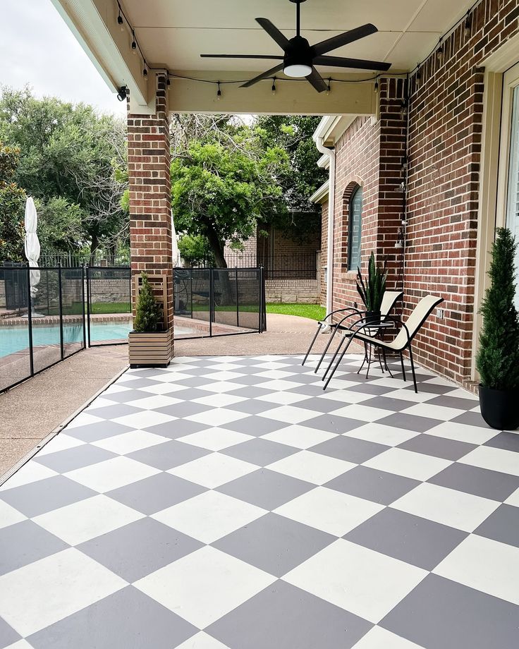 a black and white checkered tile covered porch with ceiling fan, chairs and pool