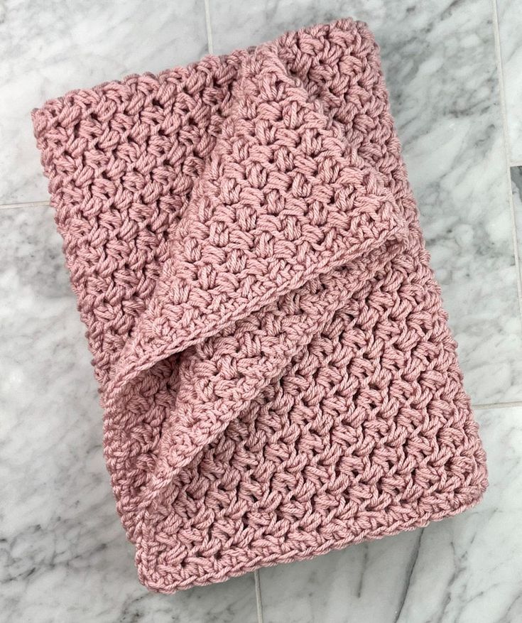 a pink crocheted blanket laying on top of a white marble tile countertop