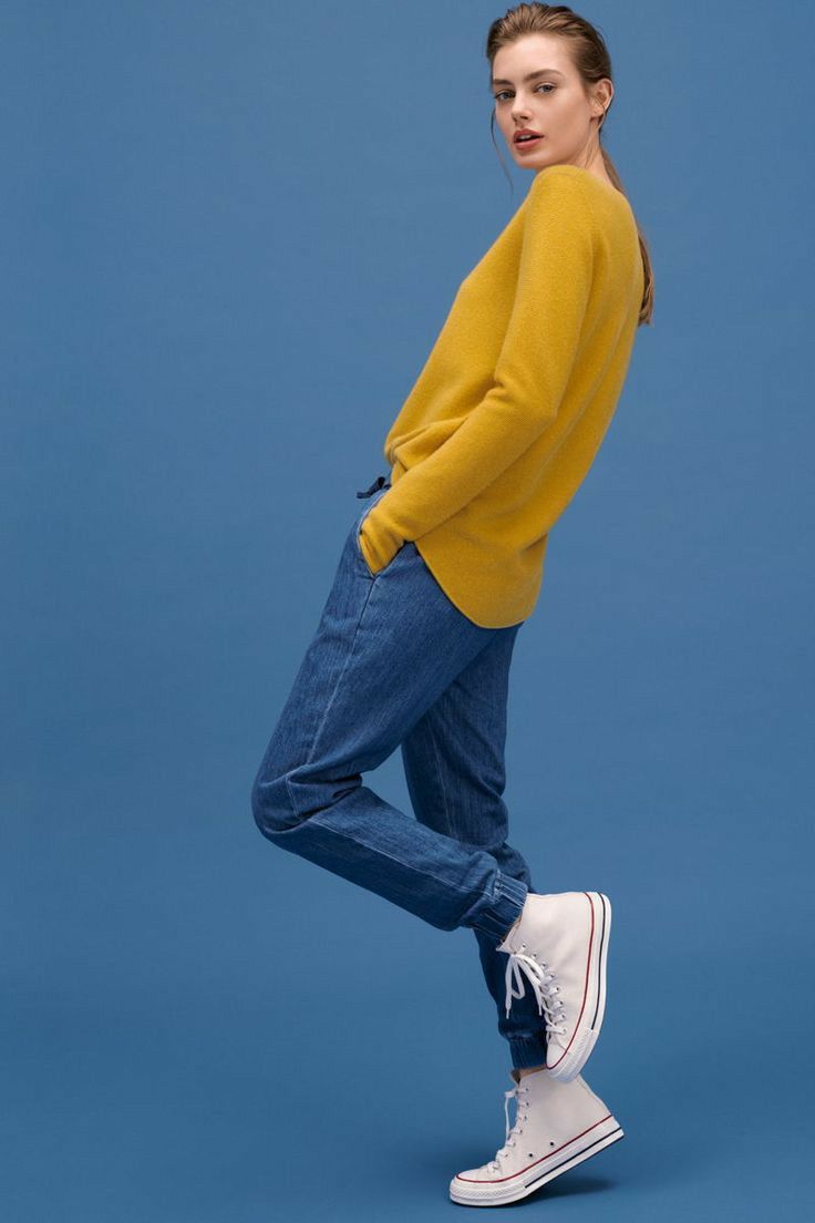 a woman in yellow sweater and jeans posing