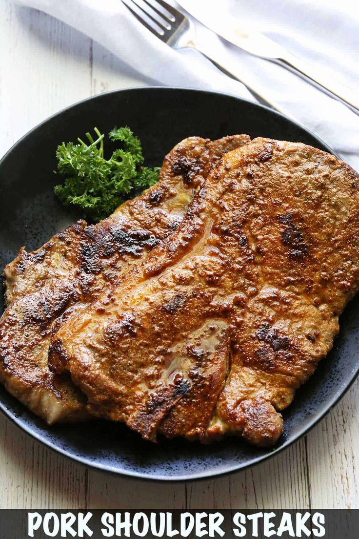 pork shoulder steaks on a black plate with broccoli and fork next to it