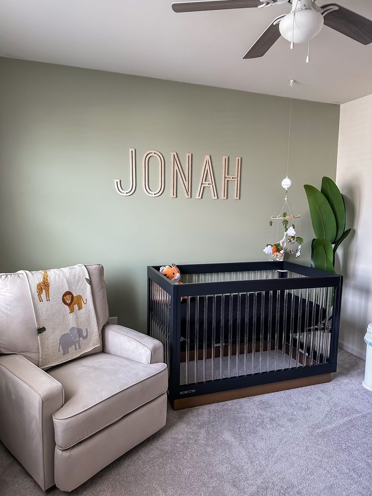 a baby's room with a crib, chair and name sign on the wall