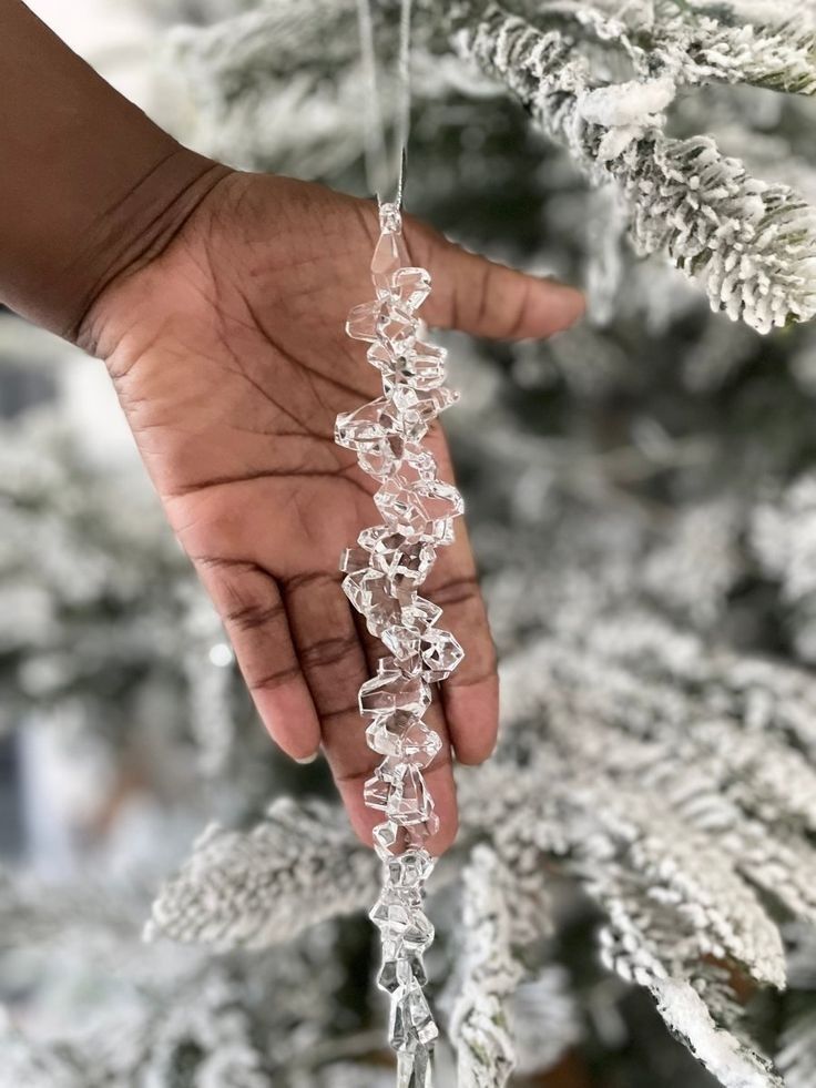 a hand is holding an ornament in front of a christmas tree with snowflakes on it