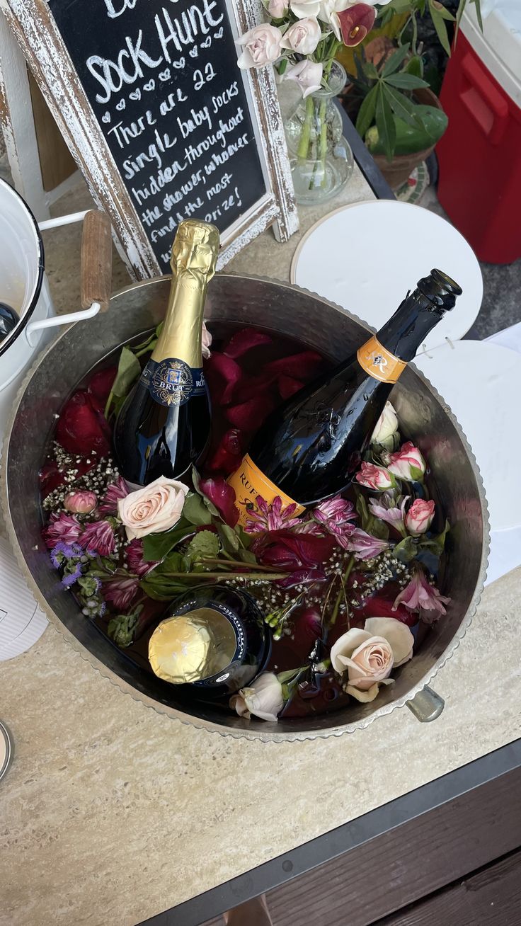 two bottles of champagne and flowers in a silver bowl with a sign on the side