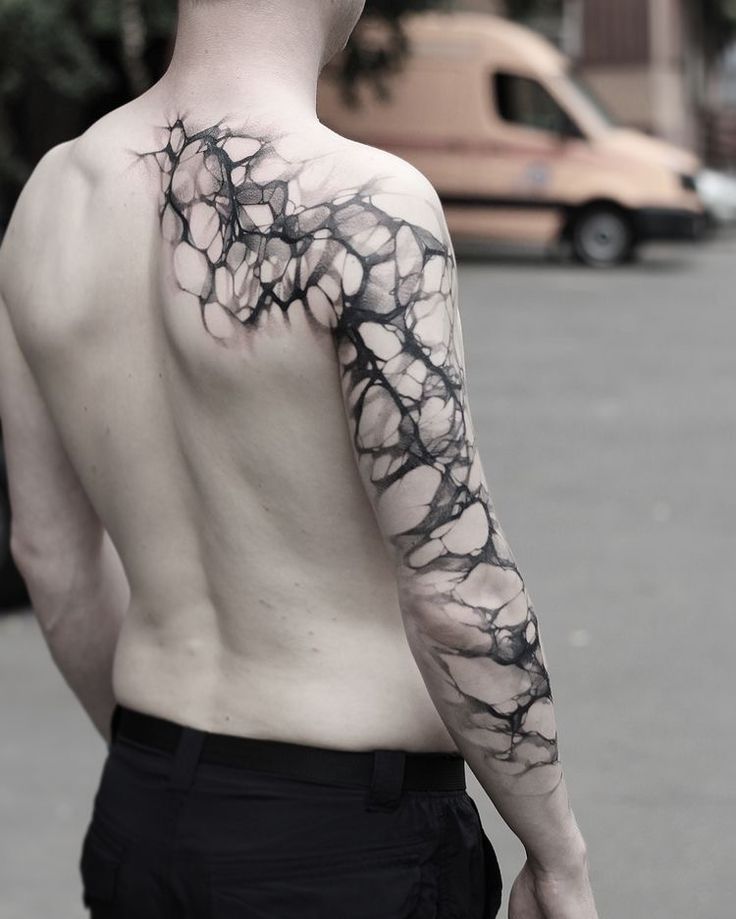 a man's back with black ink on his left arm and the top half of his body