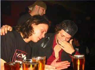 two men sitting at a table with beers in front of them and one man covering his face