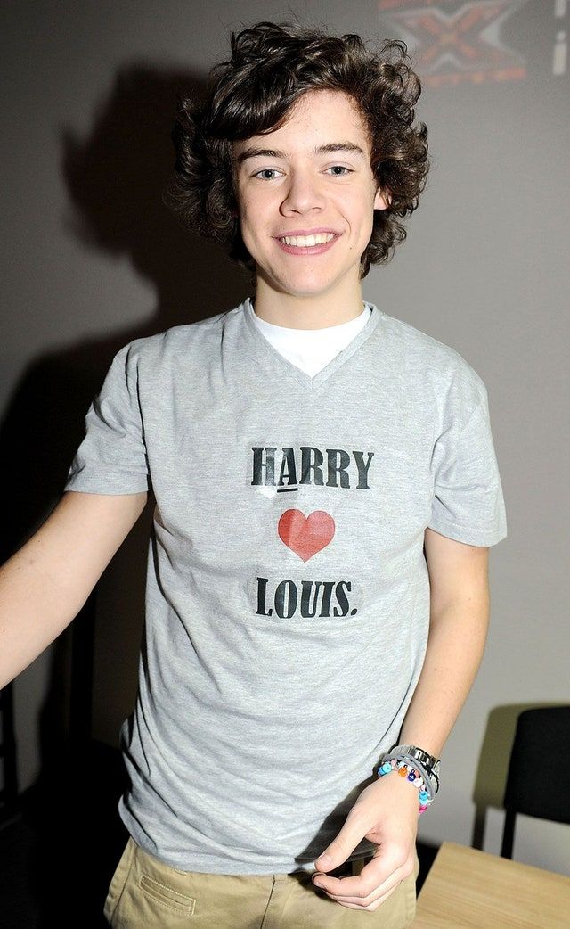 a young man with curly hair wearing a harry potter t - shirt and khaki pants