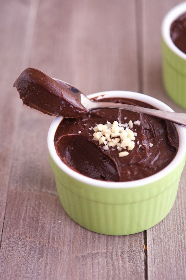 two small green bowls filled with chocolate pudding and topped with chopped nuts, on a wooden surface