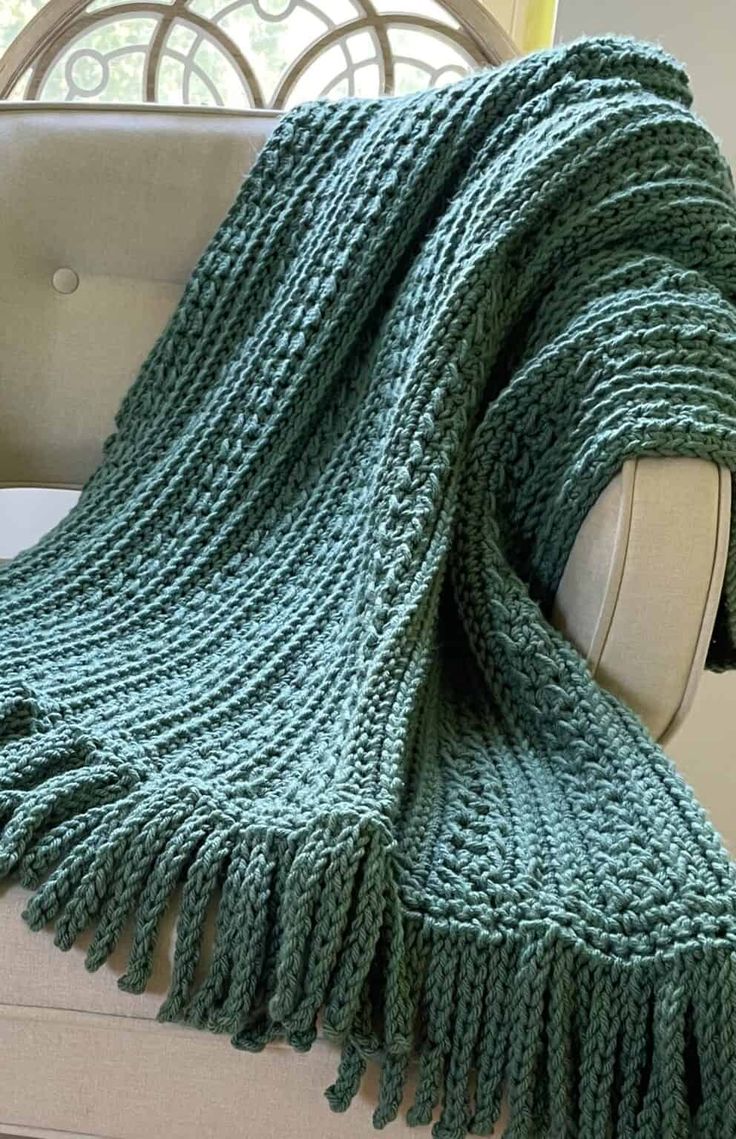 a green knitted blanket sitting on top of a couch next to a white chair