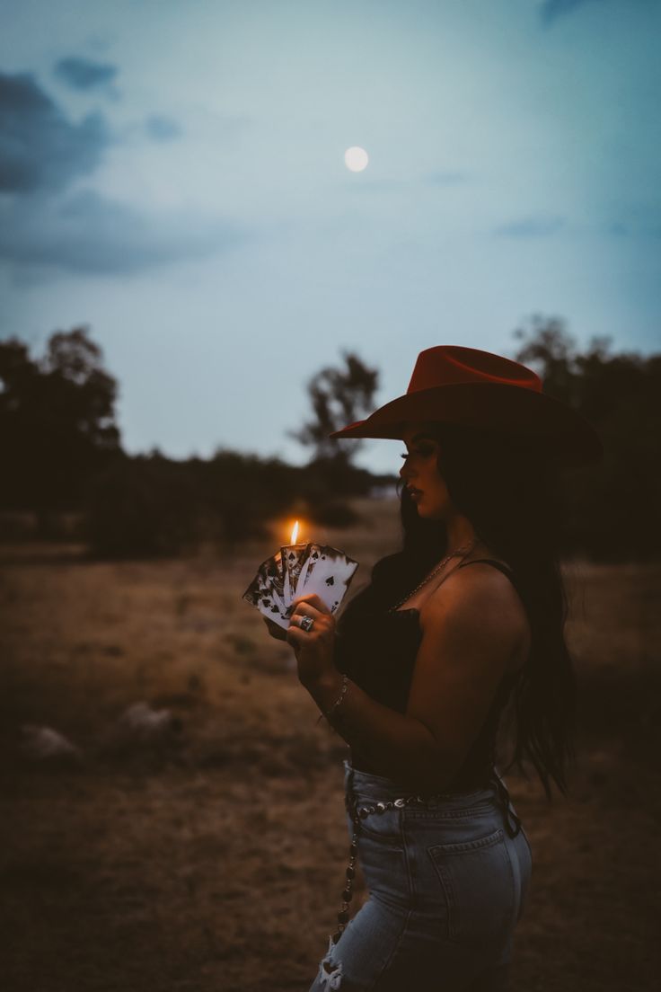 a woman wearing a cowboy hat holding a lit candle in her hand and looking at the sky