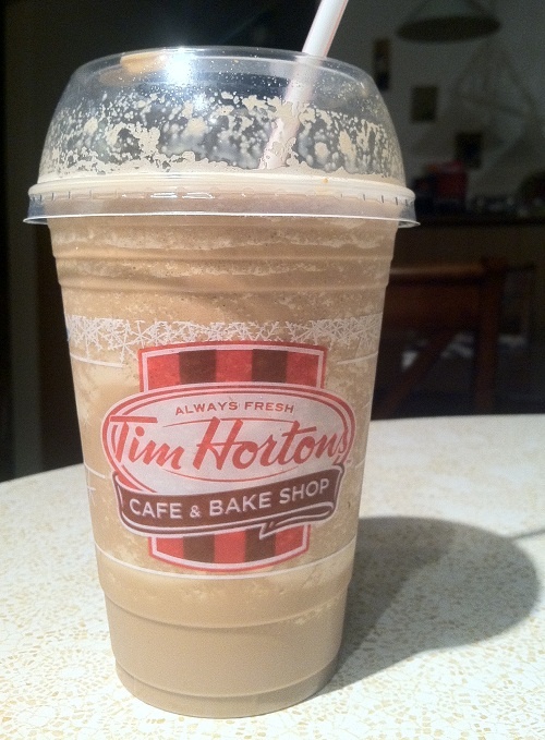 a cup with a straw in it sitting on a table next to a bottle of tim horton's coffee