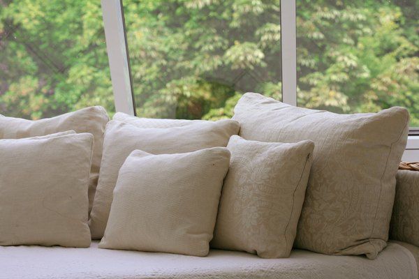 a couch with several pillows on it in front of a window and some trees outside