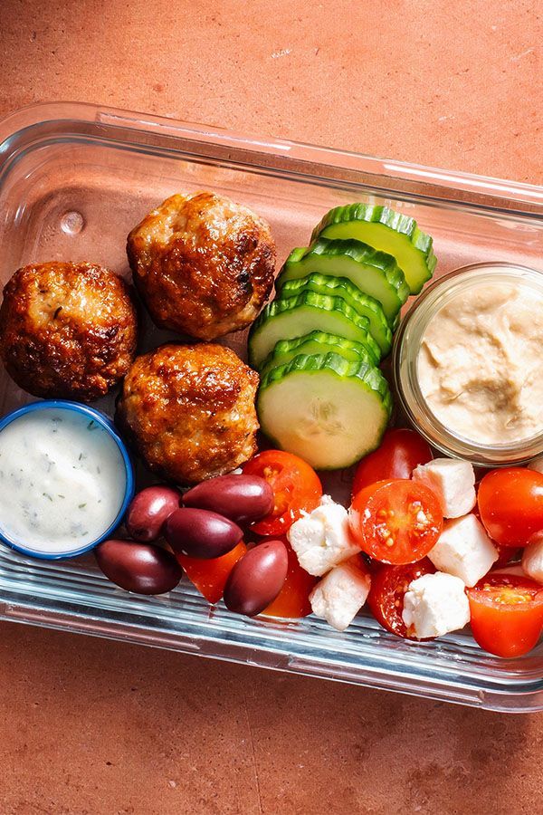 a plastic container filled with meatballs, tomatoes, cucumbers and other veggies